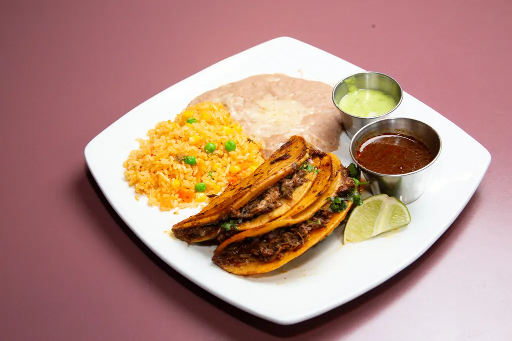 Tacos de birria con arroz, frijoles, salsa, guacamole y un gajo de limón