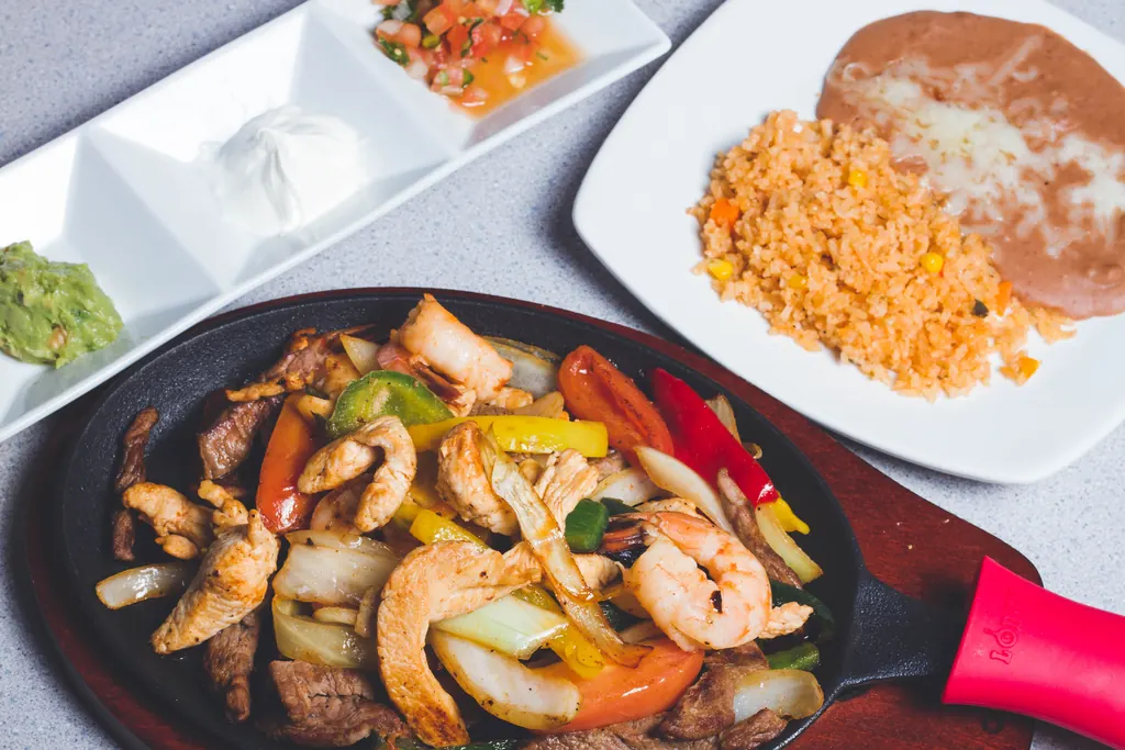 Fajitas mixtas chisporroteando, con arroz, frijoles y complementos